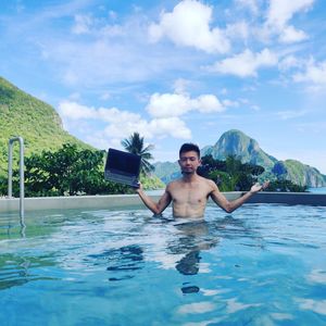 Portrait of shirtless man in swimming pool against sky