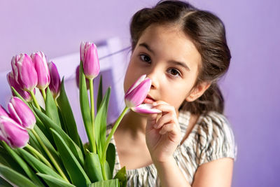 Portrait of a beautiful little girl with a bouquet of tulips, looks at the camera, purple background