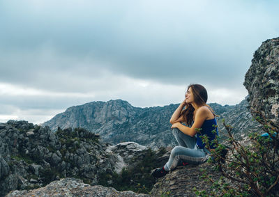 Smiling woman sitting on rock against mountain