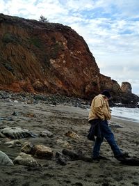 Rear view of man on rock at shore against sky