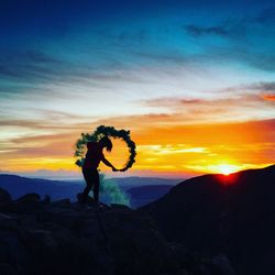 Side view of silhouette woman holding smoke bomb on mountain at sunset