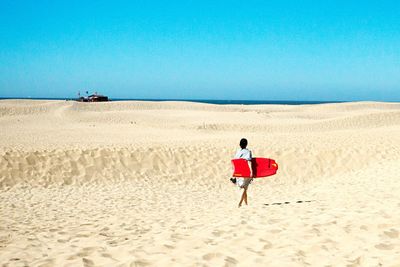 Rear view of man on sand at beach against clear blue sky