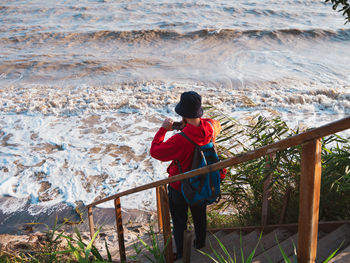 Bearded man in red hoody with backpack standing against sea with reeds. millennial guy travel alone.