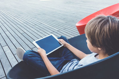 Boy using digital tablet while sitting on chair in school