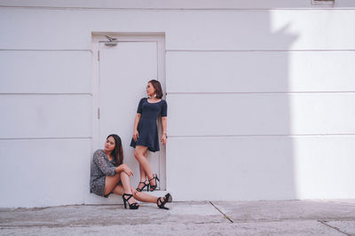 Full length portrait of woman sitting against wall