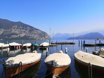 Boats moored in sea against clear blue sky in a lake surrounded by mountains.