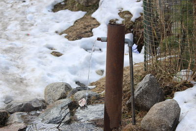 Close-up of a hand pump framed by snow on rock during winter