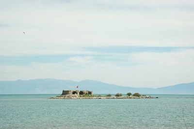 Distant view of castle amidst sea against cloudy sky