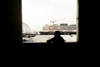 Rear view of silhouette man looking through window