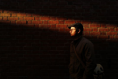 Young man standing by brick wall