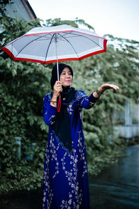 Rear view of woman with umbrella standing against wall