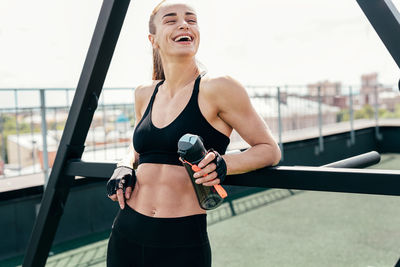 Smiling woman holding bottle while exercising in gym