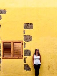 Portrait of young woman standing against yellow wall