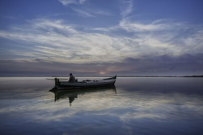 Silhouette man on boat in sea against sky during sunset