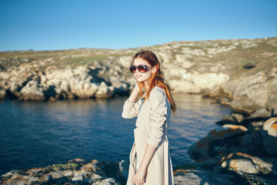 Portrait of young woman on rock against sky