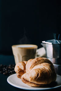 Croissant ,latte art ,and moka pot with roasted coffee on black background in the morning 