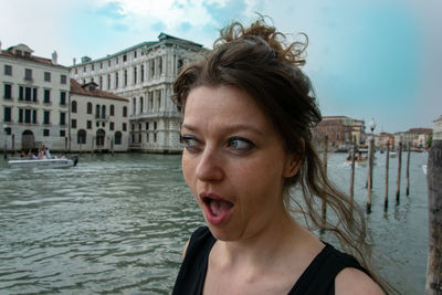 Mid adult woman with mouth open standing by canal against sky in city