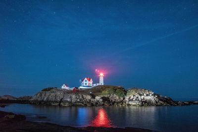 Illuminated nubble lighthouse by sea against star field