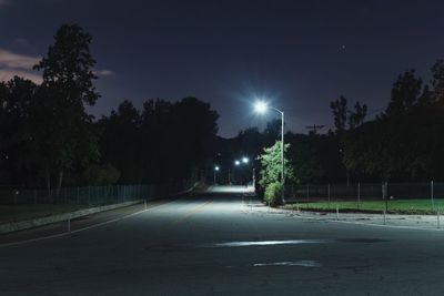 Empty road amidst trees against sky at night