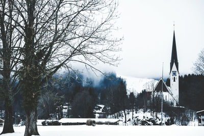 Bare trees by snow covered buildings against sky