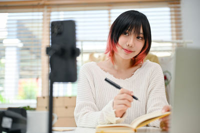 Portrait of young woman using mobile phone while sitting at home