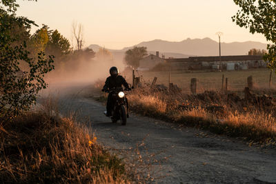 Man in leather jacket and helmet riding bike on asphalt road in sunny autumn day in countryside