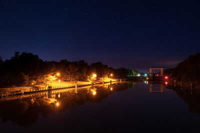 Illuminated city by lake against sky at night