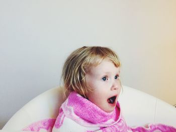 Cheerful girl wrapped in towel sitting on chair against wall at home