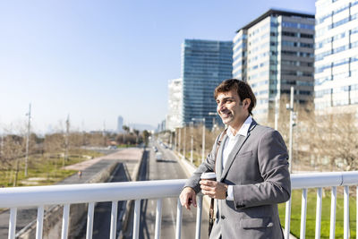Businessman having coffee while standing on bridge in city