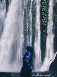 Side view of person standing by waterfall in forest