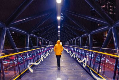 Rear view of man walking on illuminated footbridge