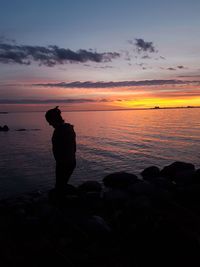 Silhouette man fishing at beach during sunset