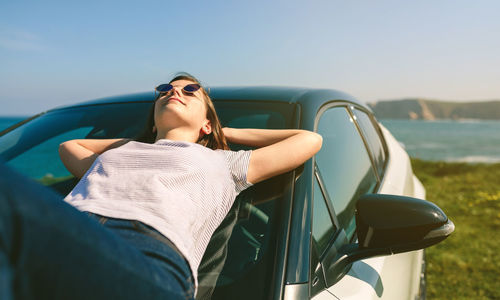 Young woman lying on car at beach