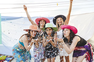 Portrait of friends blowing confetti on rooftop