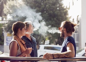Friends smoking while standing outdoors on sunny day