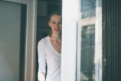 Portrait of happy young woman standing at house entrance