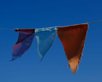 Low angle view of flags hanging against clear blue sky