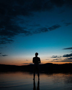 Silhouette man standing in lake against sky during sunset