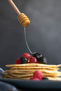 Pouring raw honey over homemade crepes on table, dark food photography