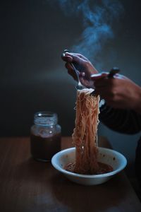 Cropped hands holding noodles at table
