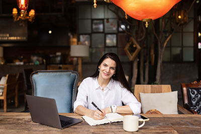 Young caucasian business woman with long brunette hair working on laptop in cafe. 