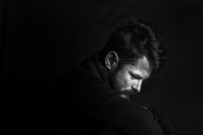 Side view of mid adult man sitting against black background