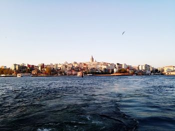 Sea and buildings in city against clear sky