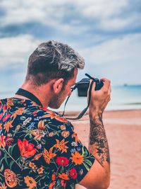 Side view of young man photographing against sky