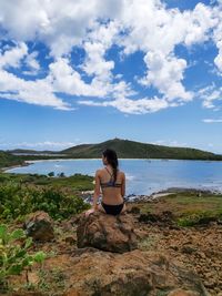 Rear view of woman wearing bikini sitting on rock