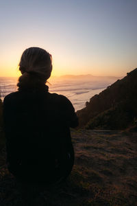 Rear view of woman looking at sea against sky during sunset