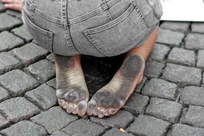 High angle view of person with dirty soles kneeling on cobbled footpath