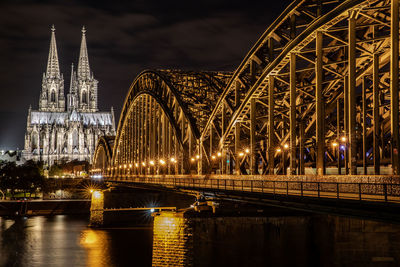 Illuminated bridge over river amidst buildings in city at night