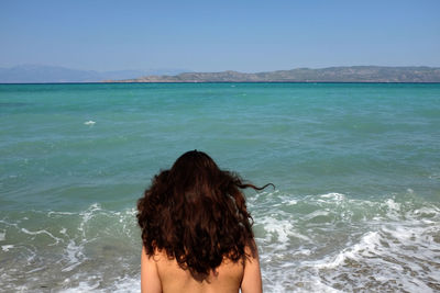 Rear view of woman standing by sea against clear sky