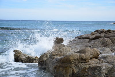 Waves splashing on rocks at shore against sky